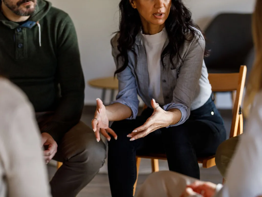Woman speaking and gesturing with her hands while seated in a small group discussion