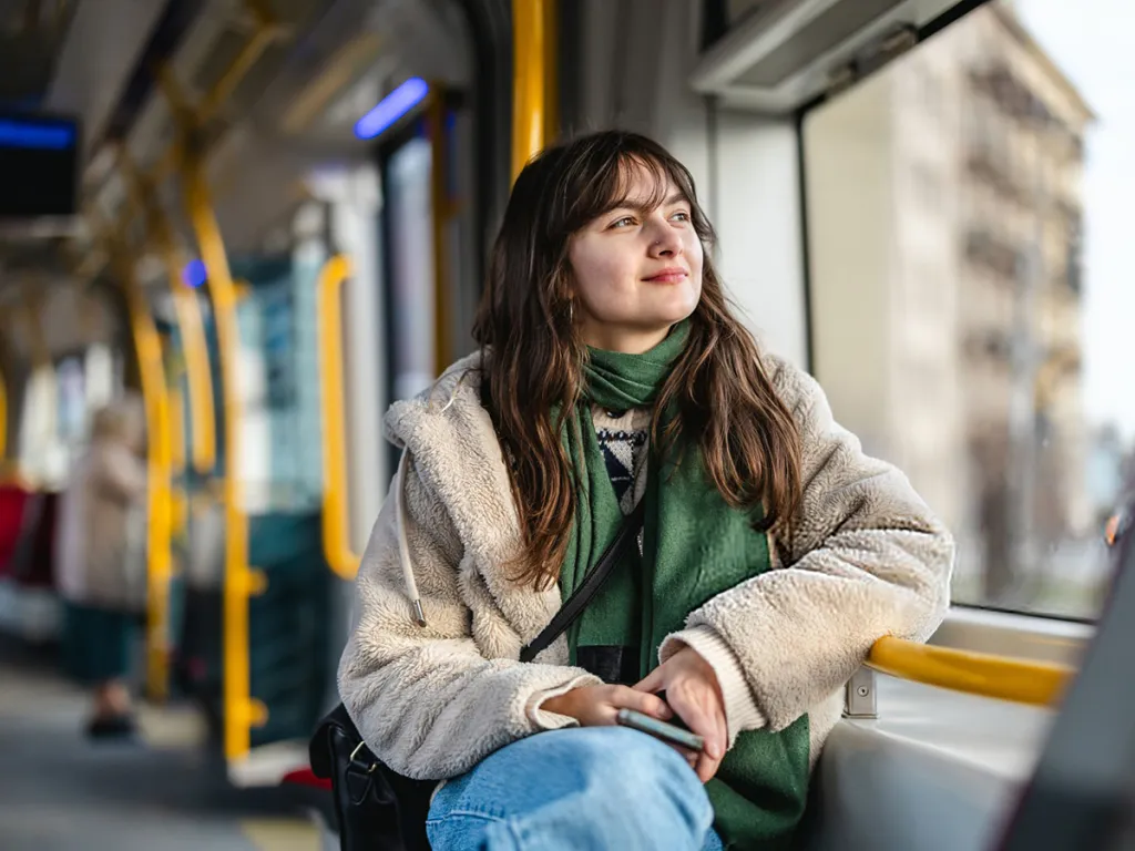 Person sitting on public transport, looking out the window while holding a phone