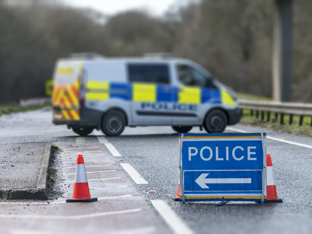 Police van blocking a road with cones and a diversion sign at a collision scene